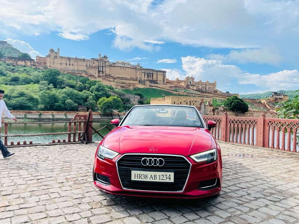 Front view of a red Audi A3 convertible parked near Amber Fort in Jaipur with scenic heritage surroundings.