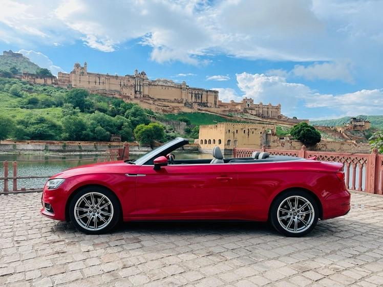 Red Audi A3 convertible parked near Jal Mahal with Amber Fort in the background in Jaipur, Rajasthan.