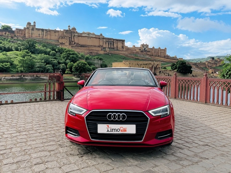 Front view of a red Audi A3 convertible parked near Amber Fort with Limo Car India branding.