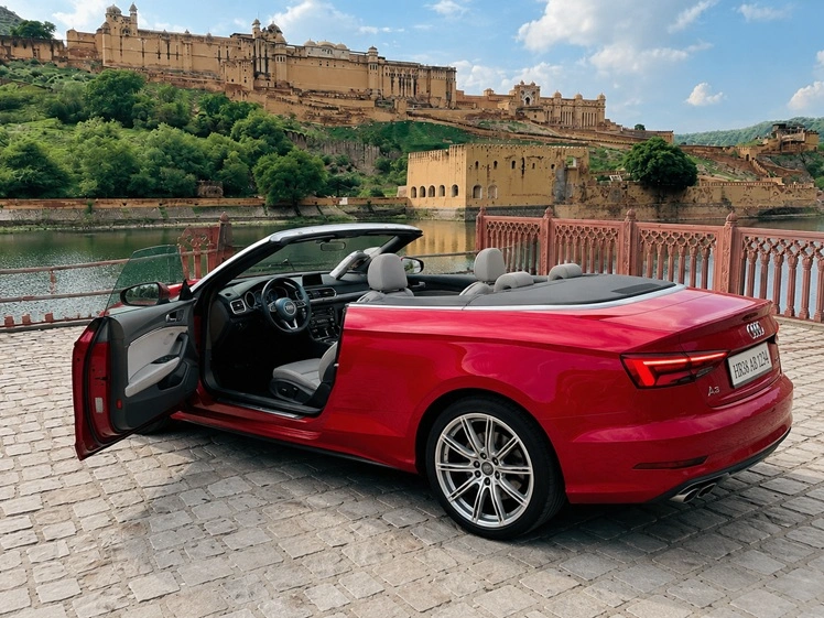 Red Audi A3 convertible with driver-side door open overlooking Amber Fort in Jaipur.