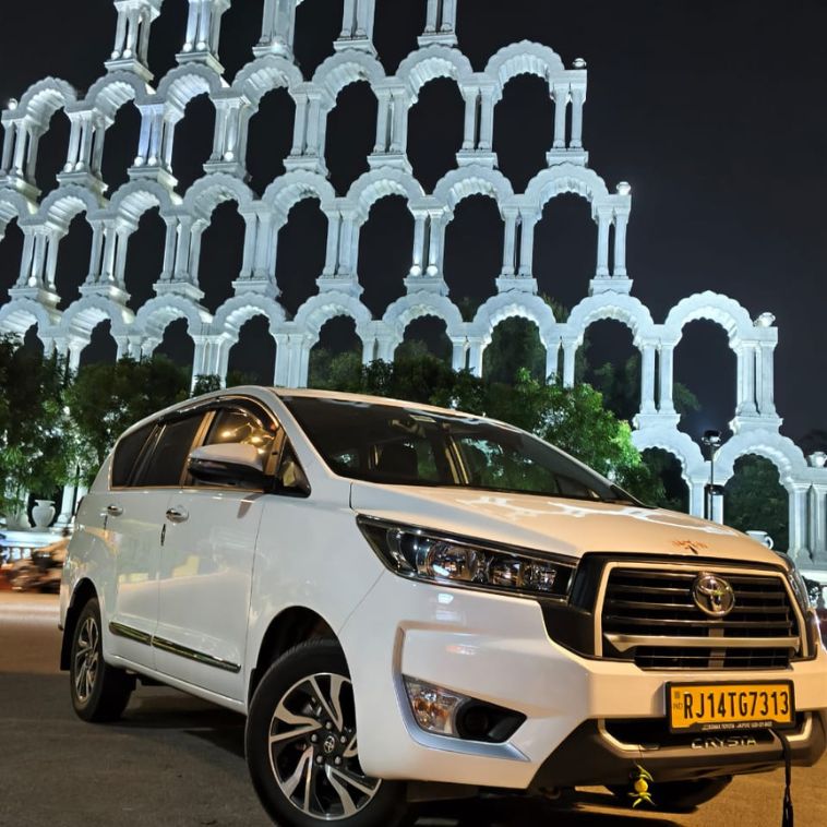White Toyota Innova Crysta parked at Patrika Gate in Jaipur at night, representing Limo Car India's premium taxi and sightseeing services.