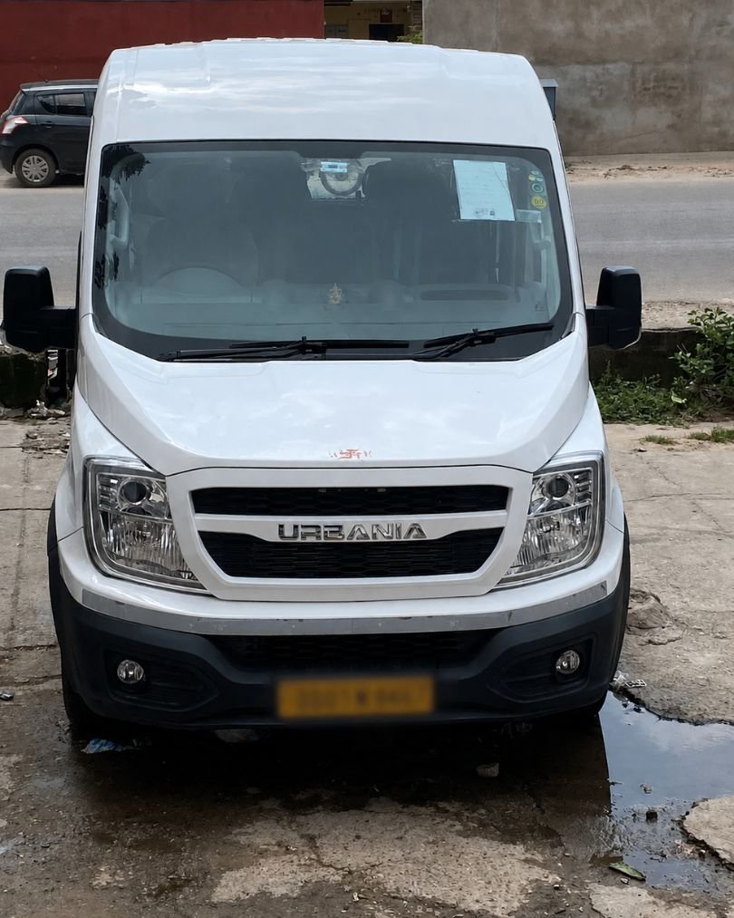 Force Urbania luxury 17-seater van parked outside showroom for group travel and rental service.